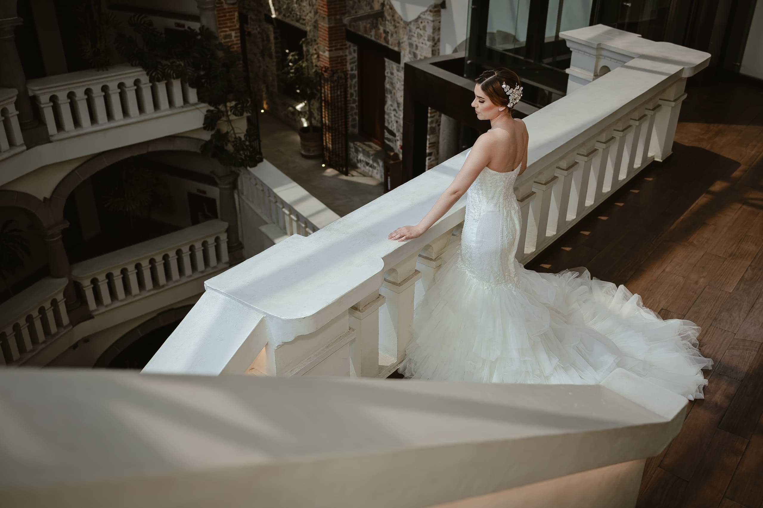 Novia recorre la escalinata de una casona con barandales blancos y patio de piedra