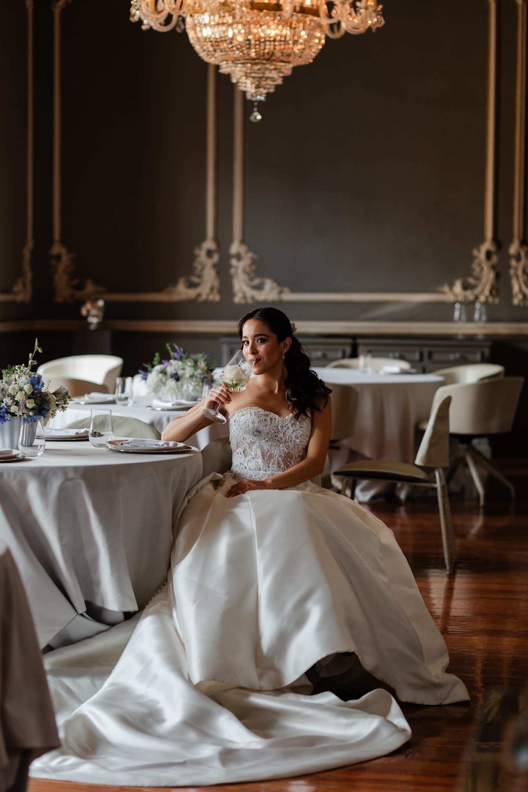 Novia sentada a una mesa vestida en un salón de gala en penumbra
