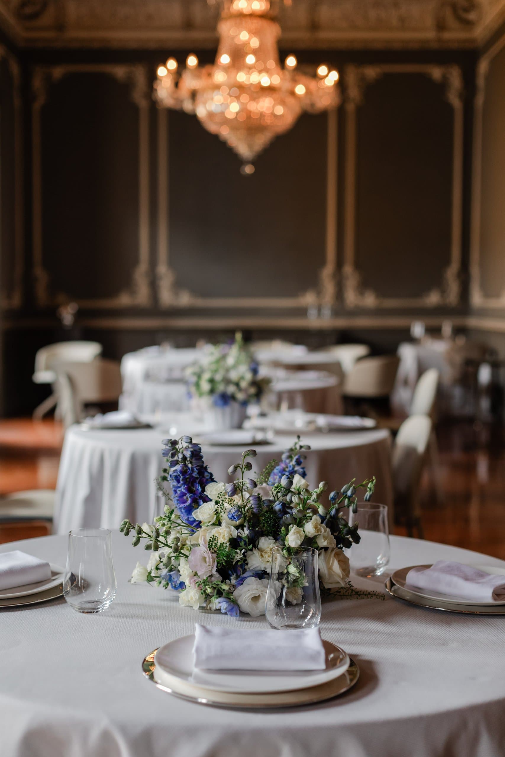 Mesa redonda con centro de flor azul y blanca bajo el candil de un salón de palacio