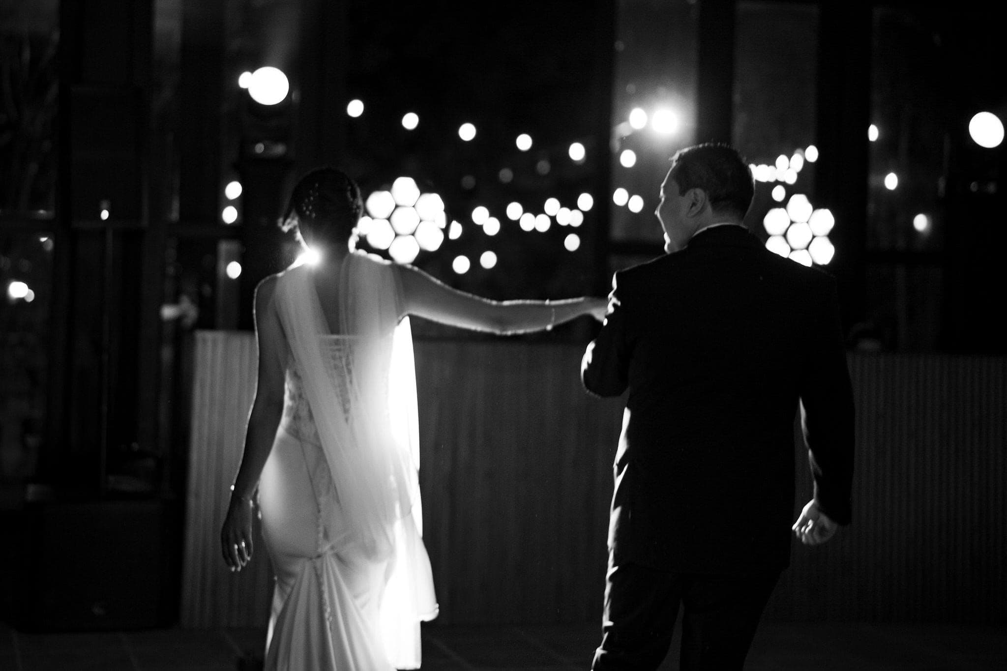 Pareja caminando bajo series de luces cálidas, en blanco y negro
