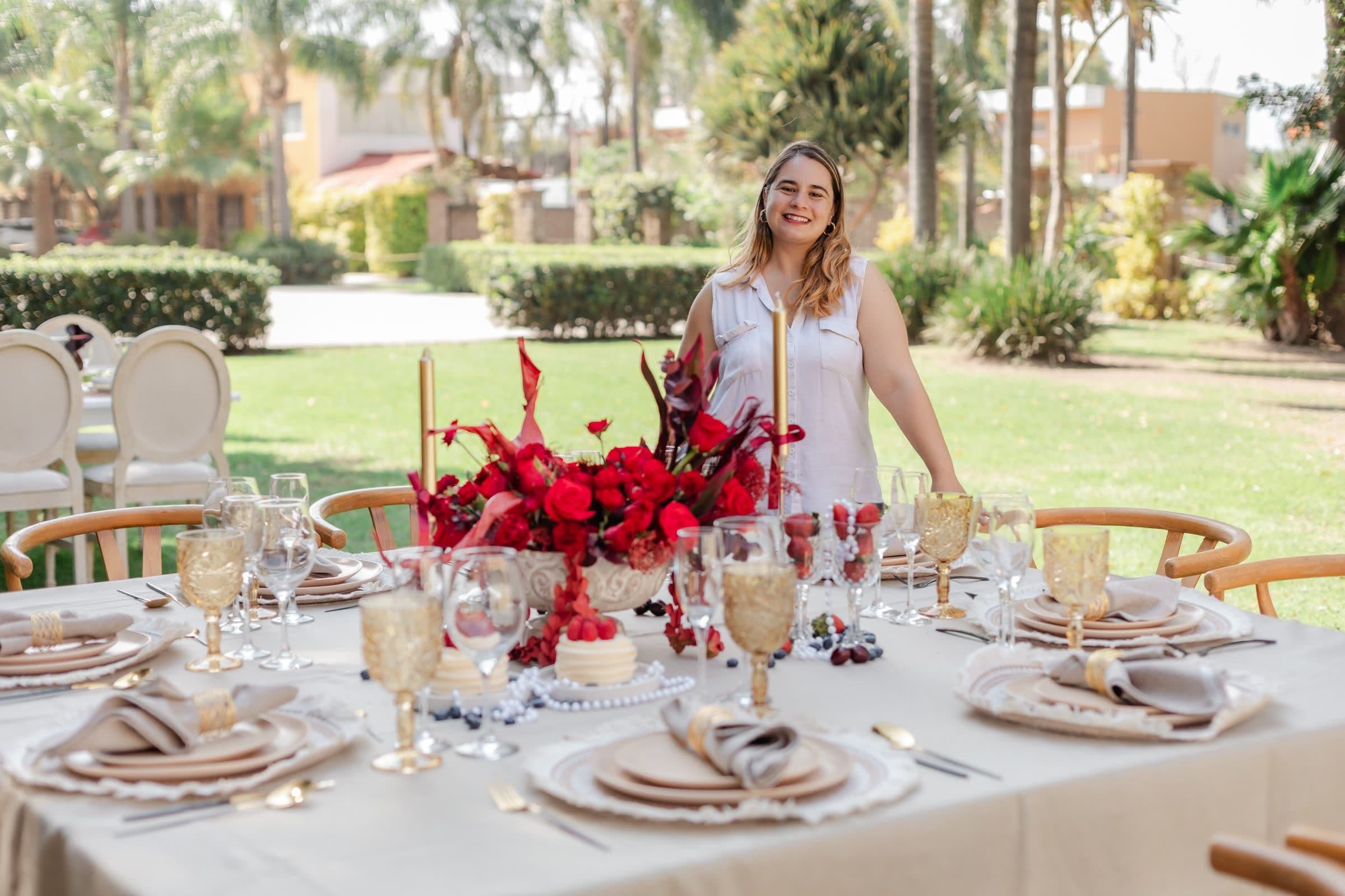 Tania of Clhei beside a styled table with a red-toned floral centerpiece, in a garden in Puebla