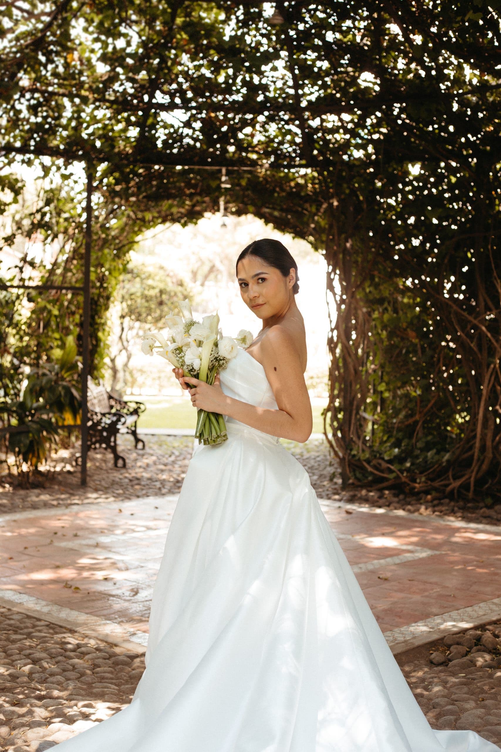 Novia bajo un arco de vegetación con su ramo, en una boda coordinada por Clhei