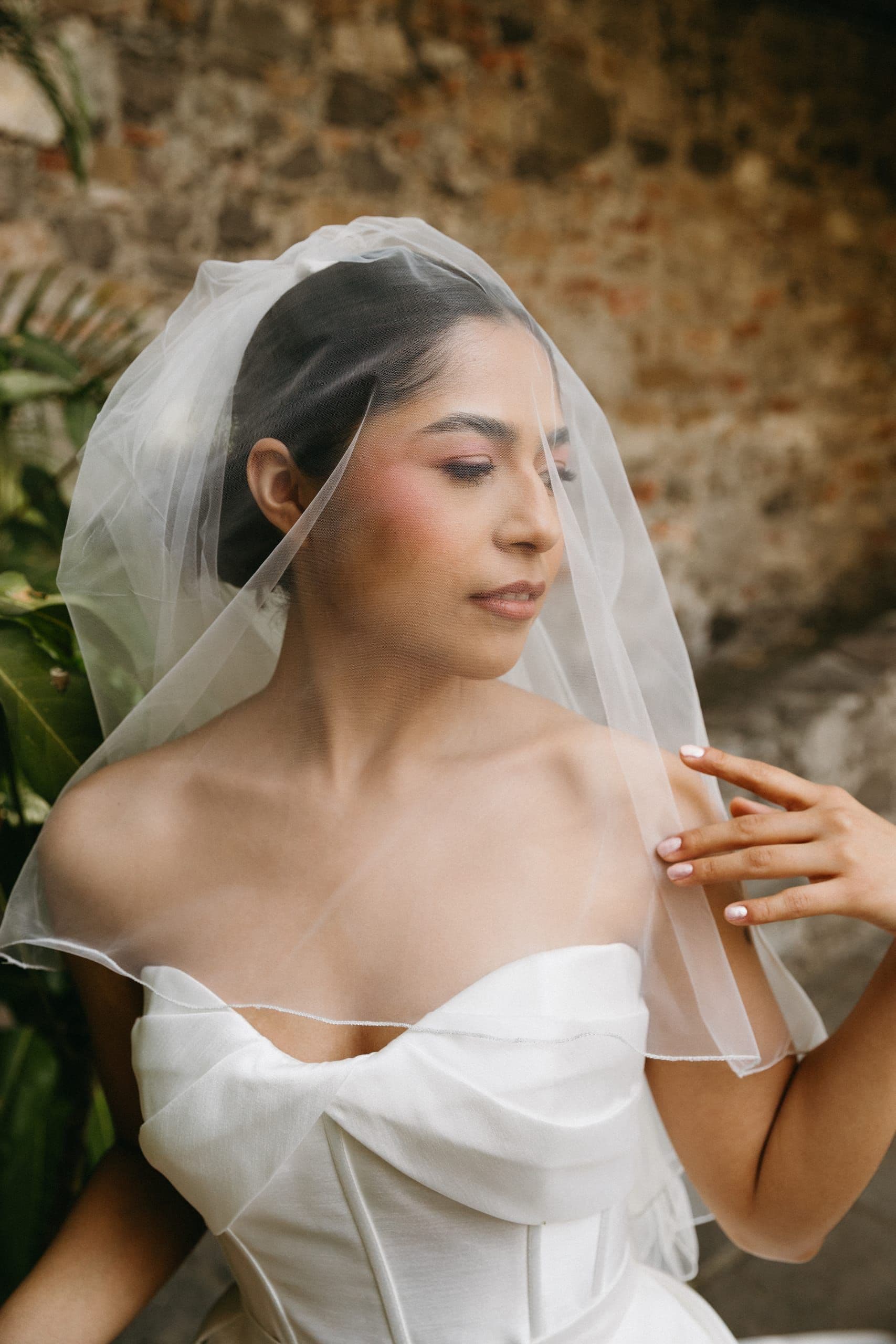 Retrato de novia ajustando su velo, con vestido de escote off-shoulder