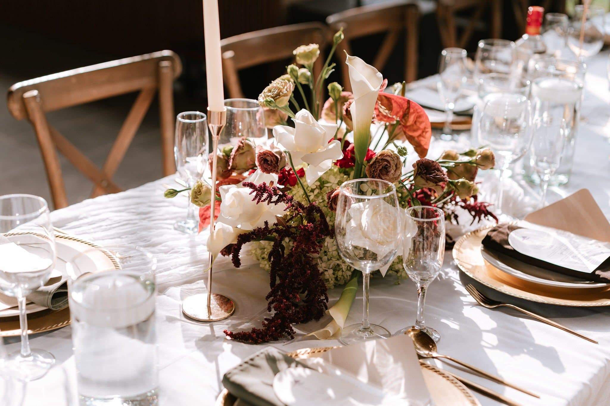 Centro de mesa con calas, orquídeas vino y flor blanca sobre mantelería clara