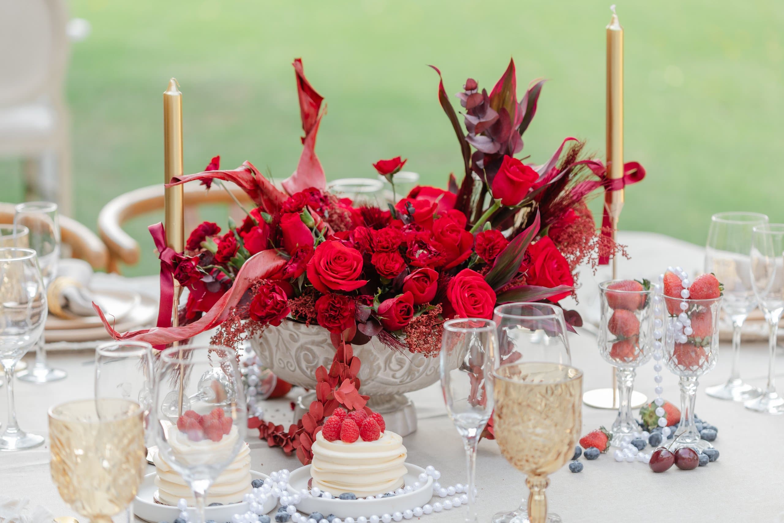 Centro de mesa en rojo con rosas y anturios, junto a un pastel y copas doradas
