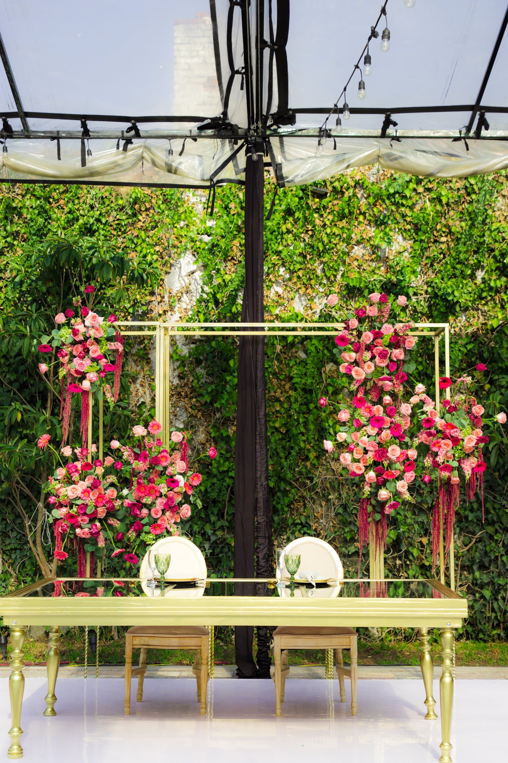 Mesa de novios frente a un muro verde con marco dorado y buganvilia fucsia