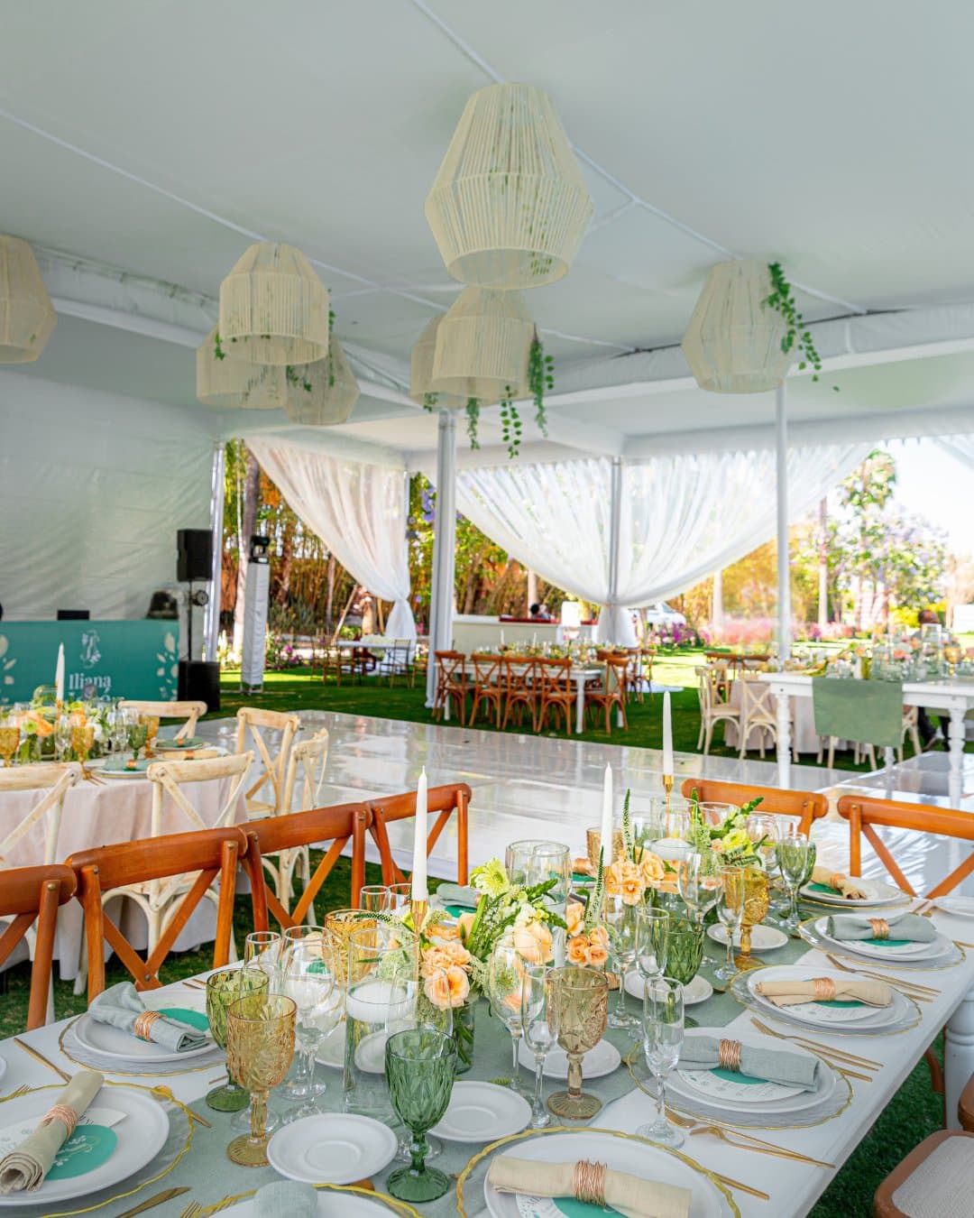 Banquete bajo carpa con lámparas de papel y mesas en tonos durazno y verde