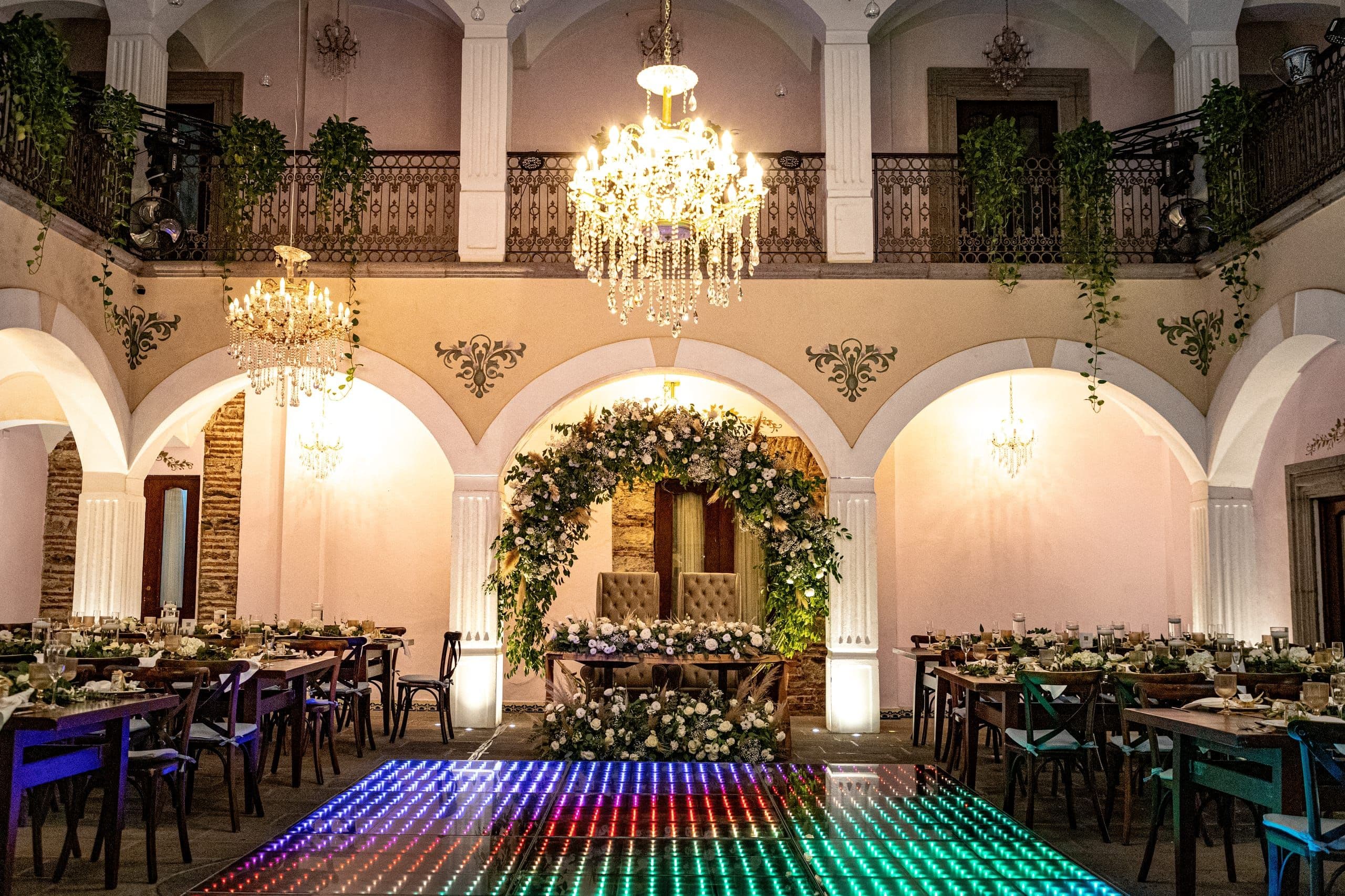 Patio de hacienda con candil, arco floral y pista iluminada, ambientación de Clhei
