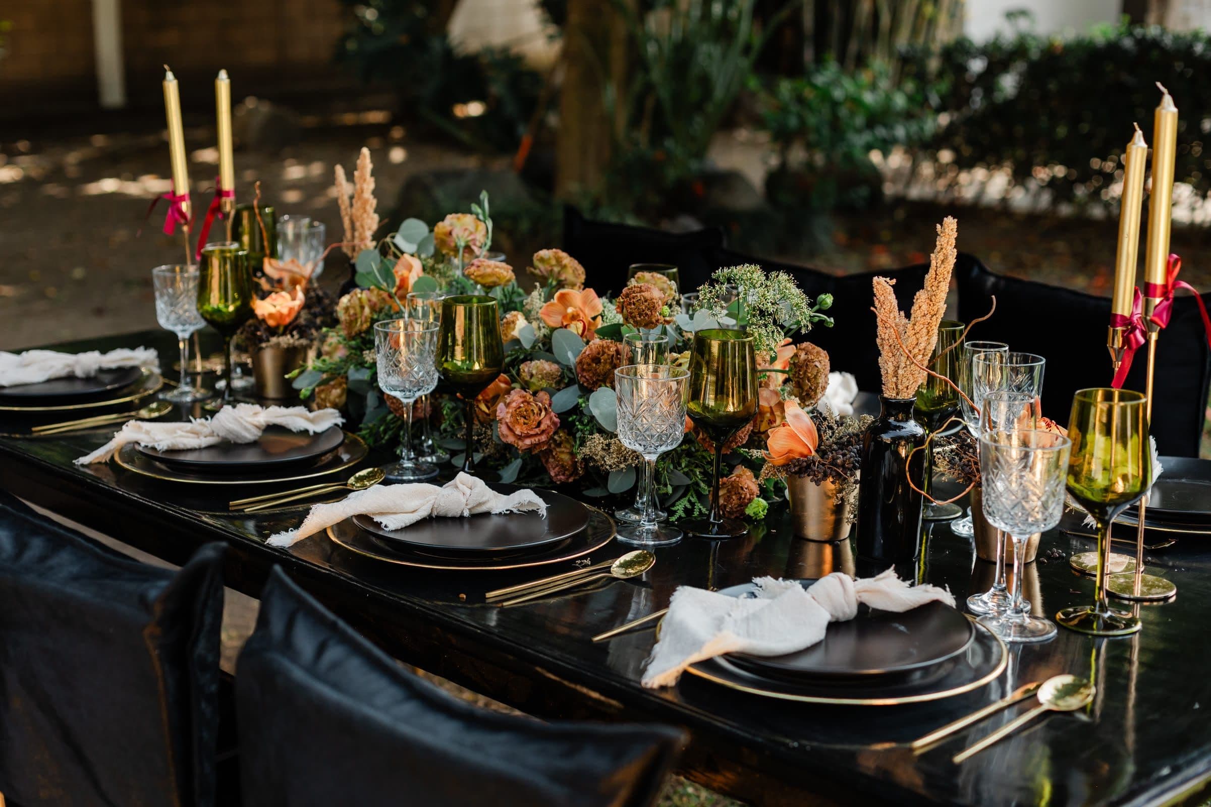 Mesa de boda en tonos oscuros con flores en tonos secos, rosas toffee y velas doradas