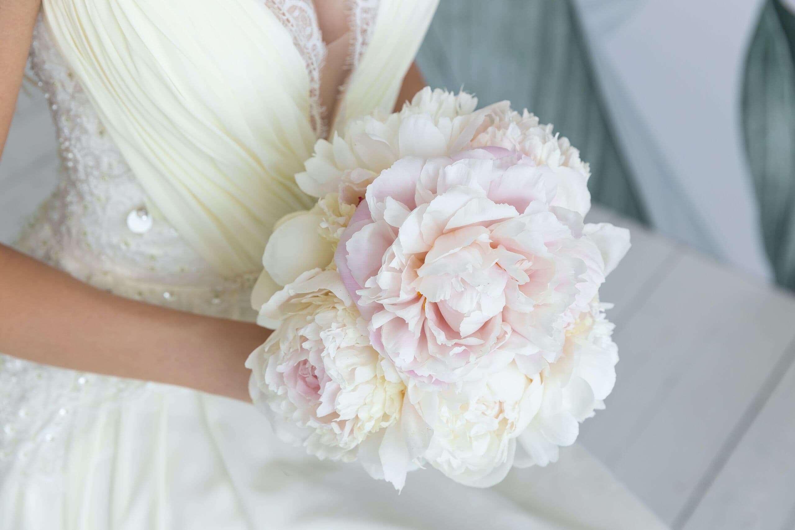 Ramo de peonías en tonos crema y rosa pálido sostenido sobre un vestido de novia