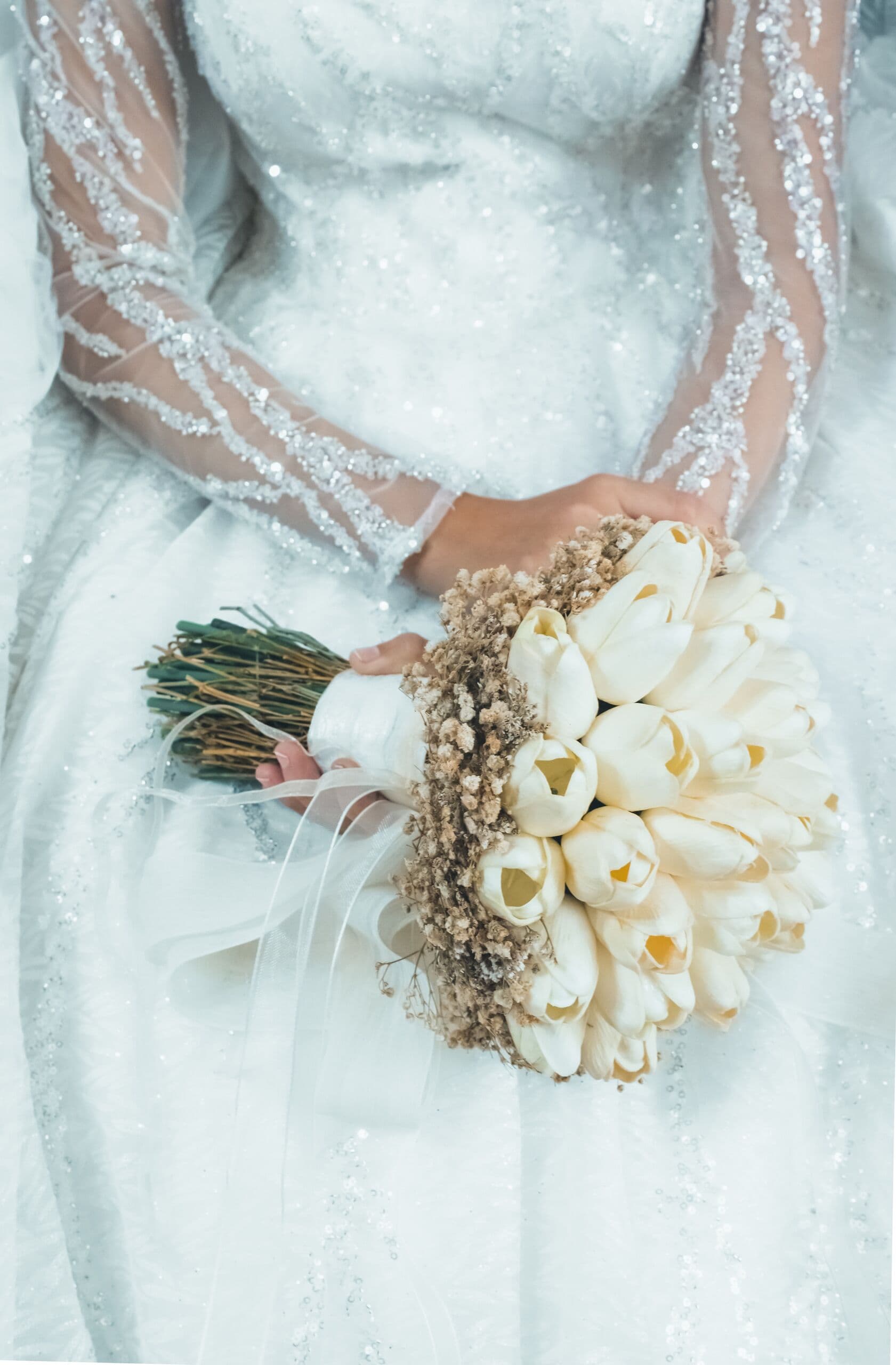 Ramo de tulipanes blancos con acentos secos en manos de una novia con mangas de encaje