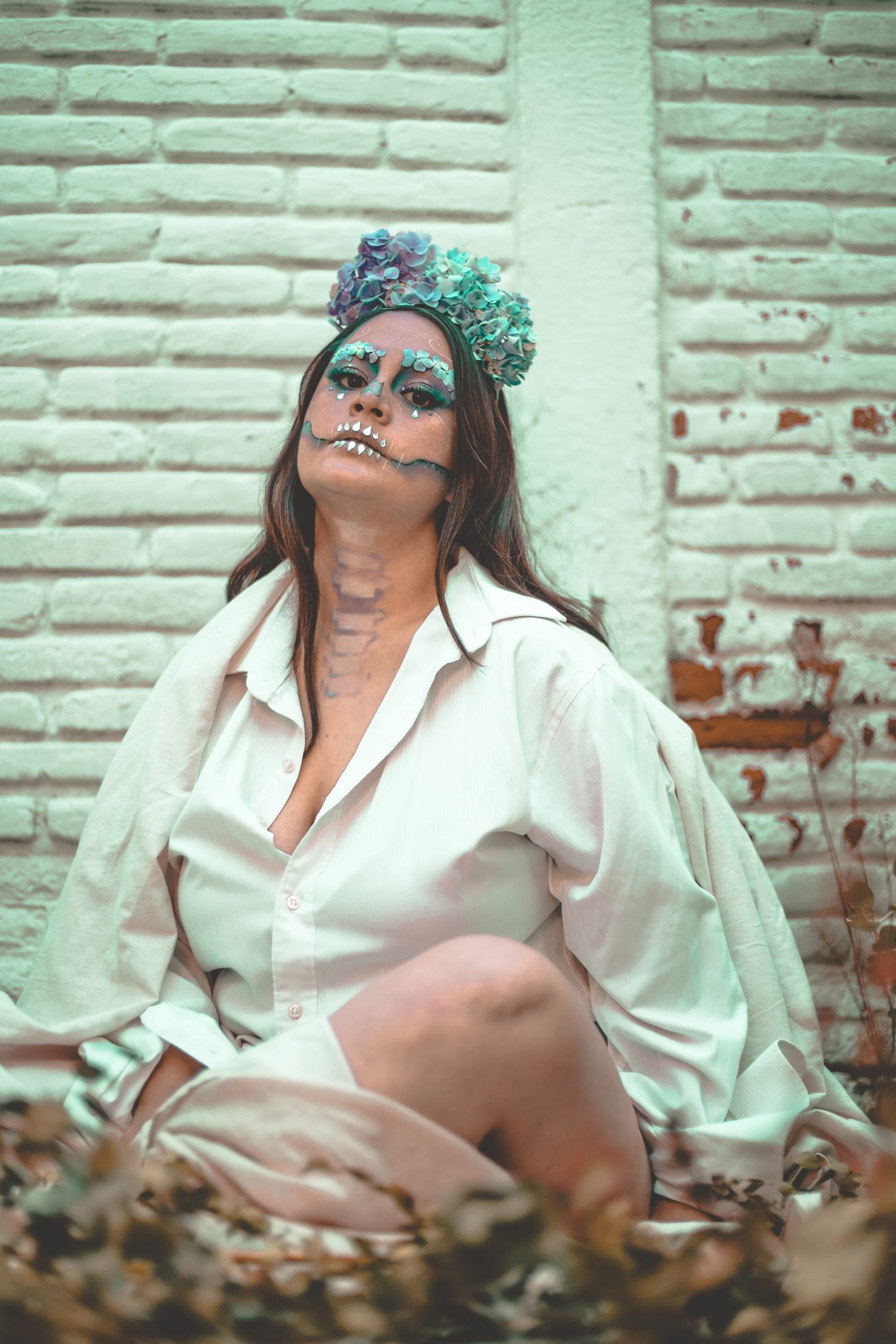 Catrina de camisa blanca sentada junto al muro de ladrillo