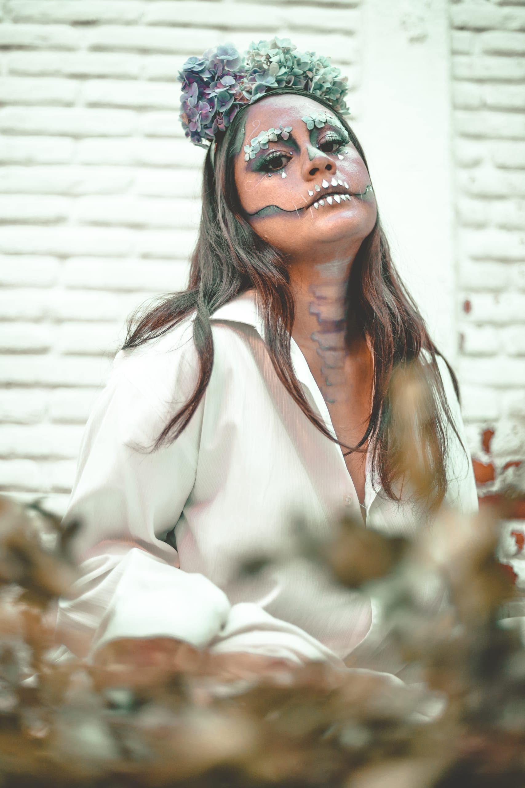 Retrato de catrina con corona azul sobre muro de ladrillo blanco