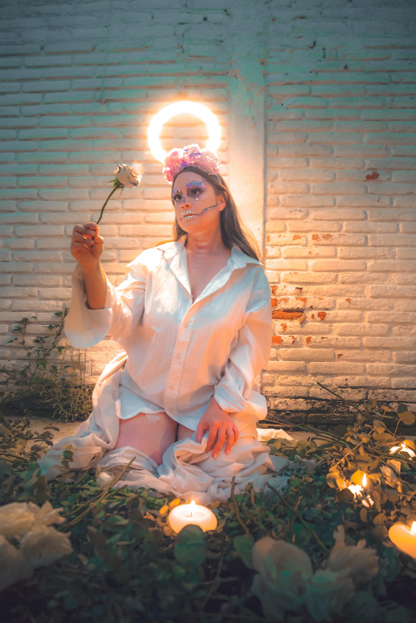 Catrina con halo de luz sosteniendo una rosa entre velas