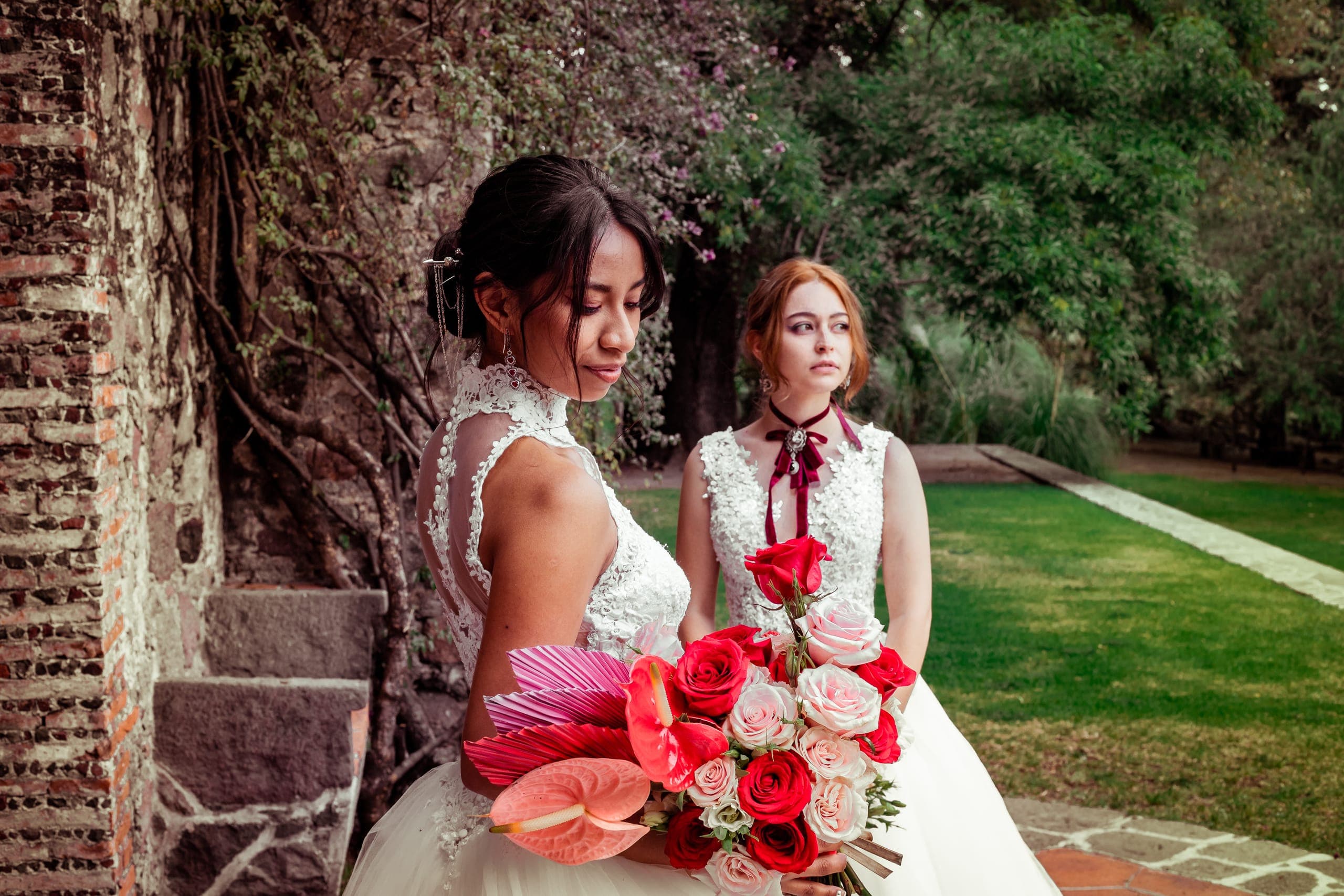 Dos novias con ramos en tonos rojos y rosas en el jardín de la hacienda