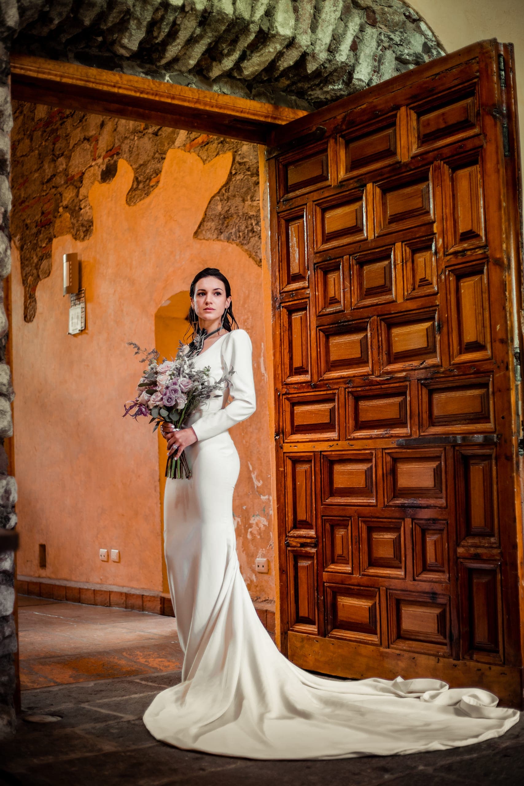 Novia en el umbral de una puerta de madera tallada, vestido de corte sirena