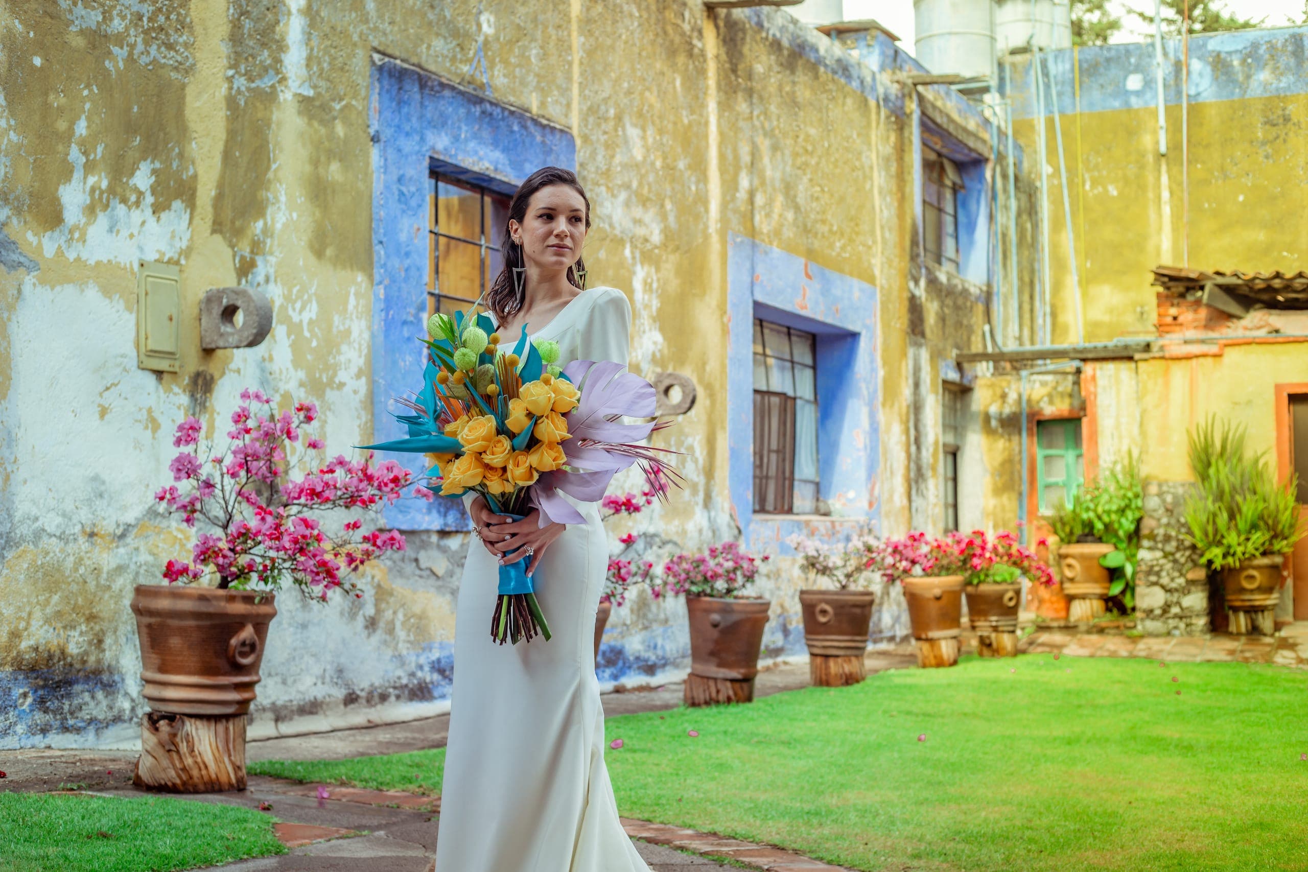Novia con ramo tropical en amarillos y rosas en el patio de la hacienda