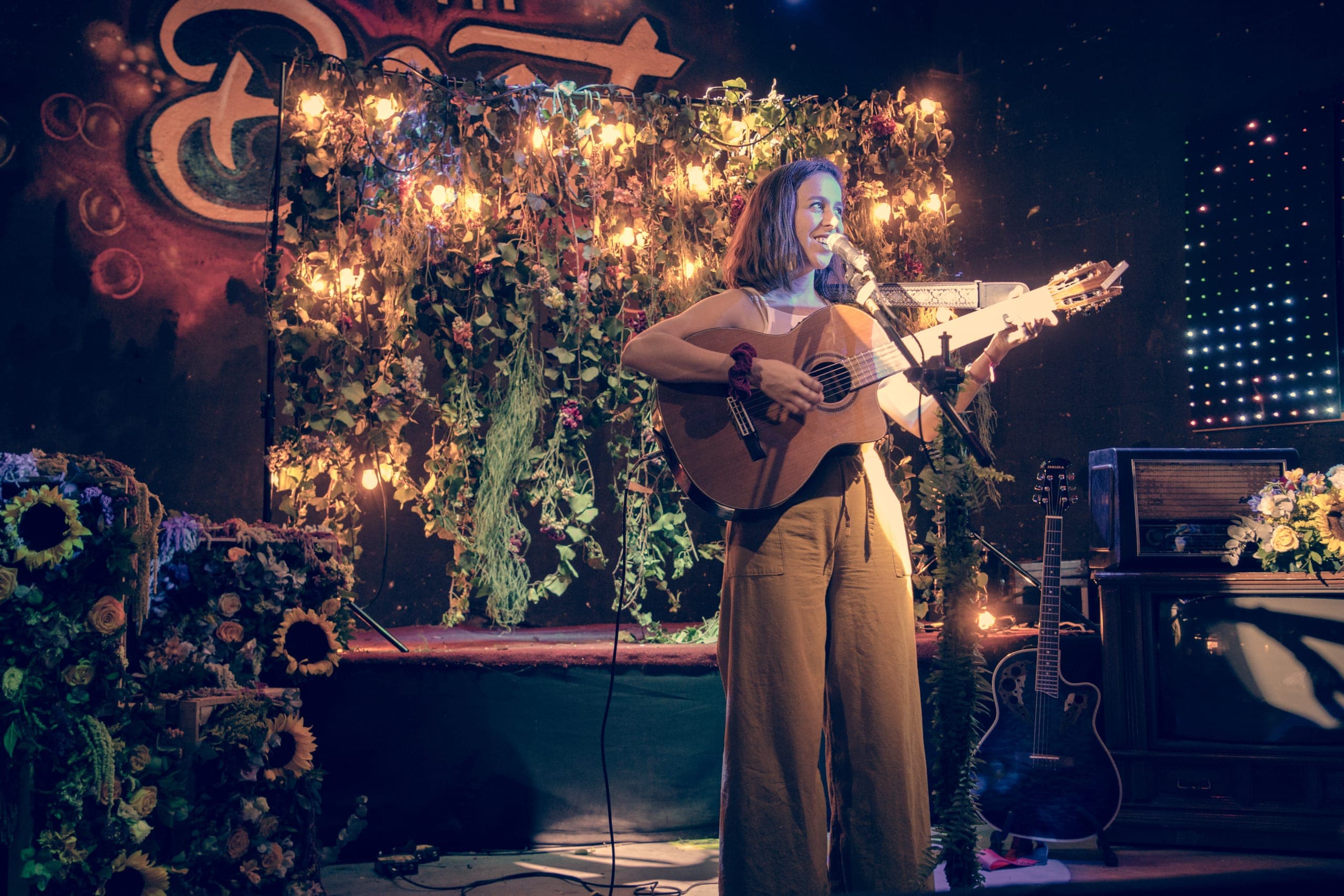 Cantante con guitarra sobre el escenario cubierto de flor y follaje
