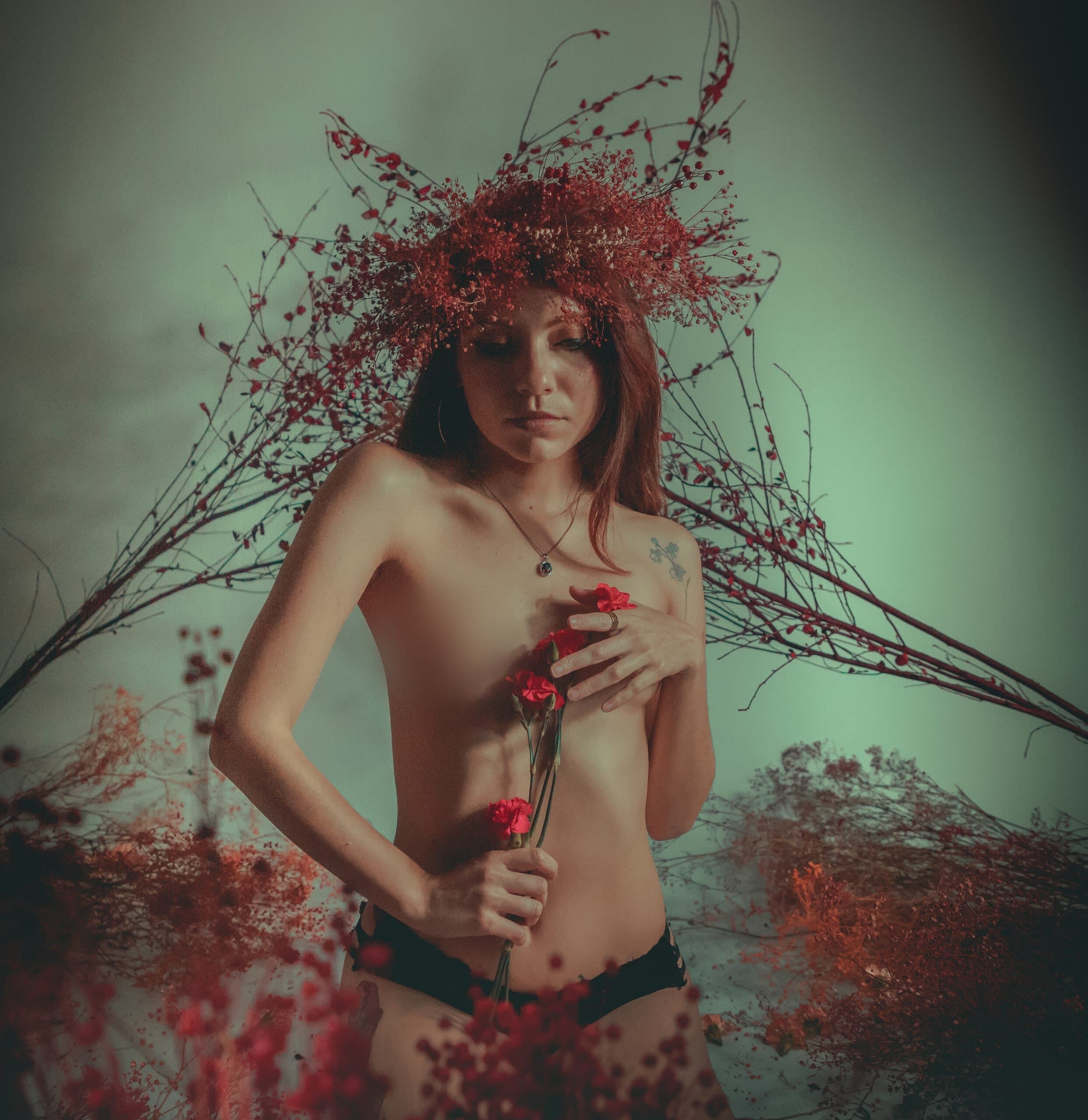 Retrato con corona roja y claveles en mano entre ramas de flor seca
