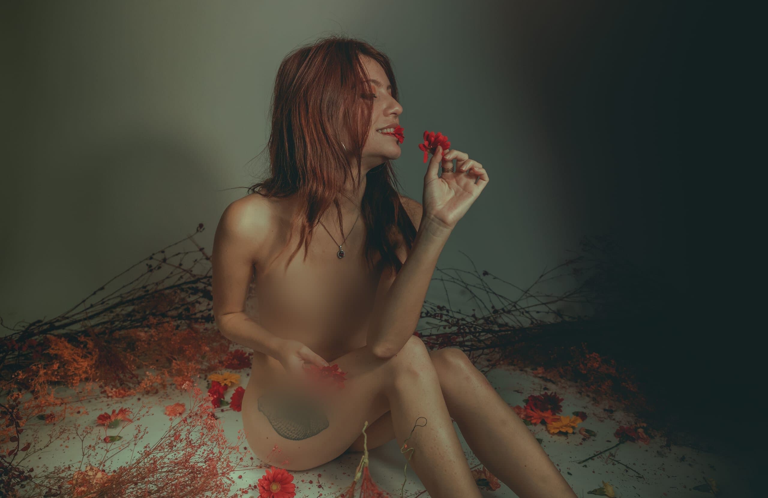 Retrato sentado con flor roja entre los dedos, luz baja de estudio