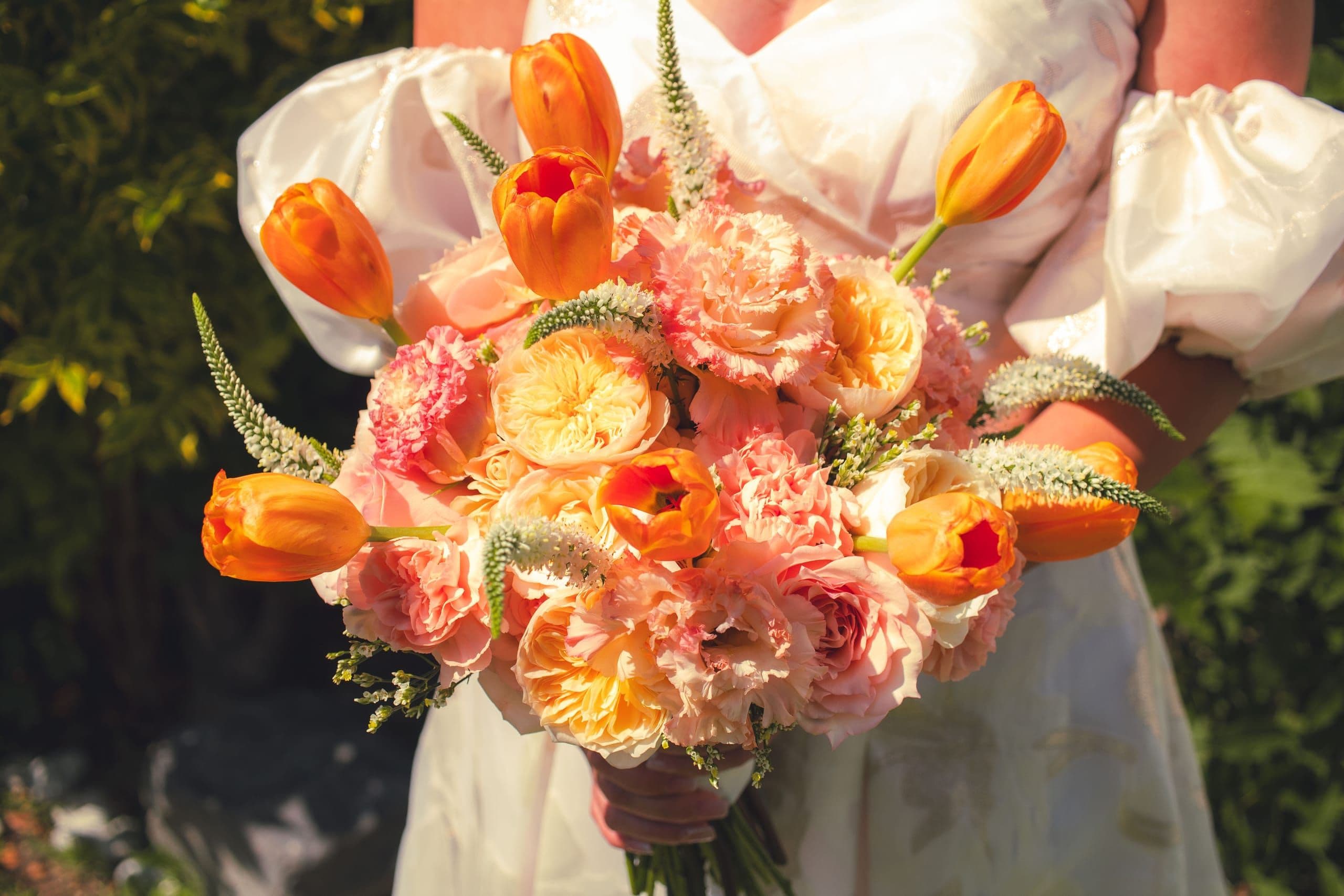Ramo de tulipanes naranjas y rosas de jardín durazno en manos de una novia
