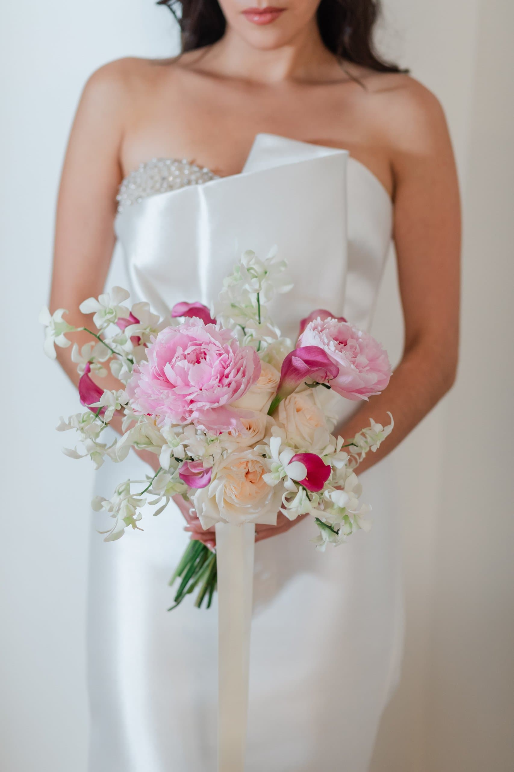 Ramo de peonías rosas y ranúnculos blancos sobre vestido de novia liso