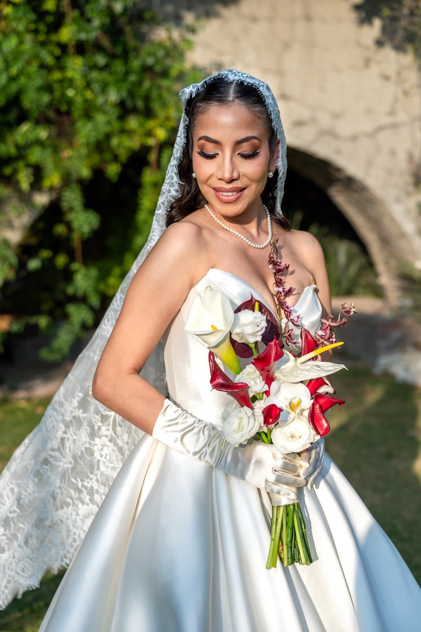 Novia con mantilla sosteniendo un ramo de calas blancas y orquídeas vino