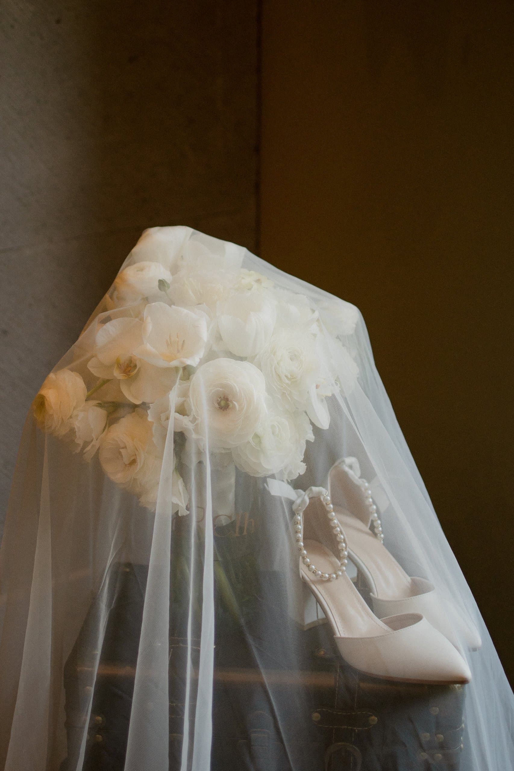 Ramo de ranúnculos blancos y zapatillas de novia bajo el velo