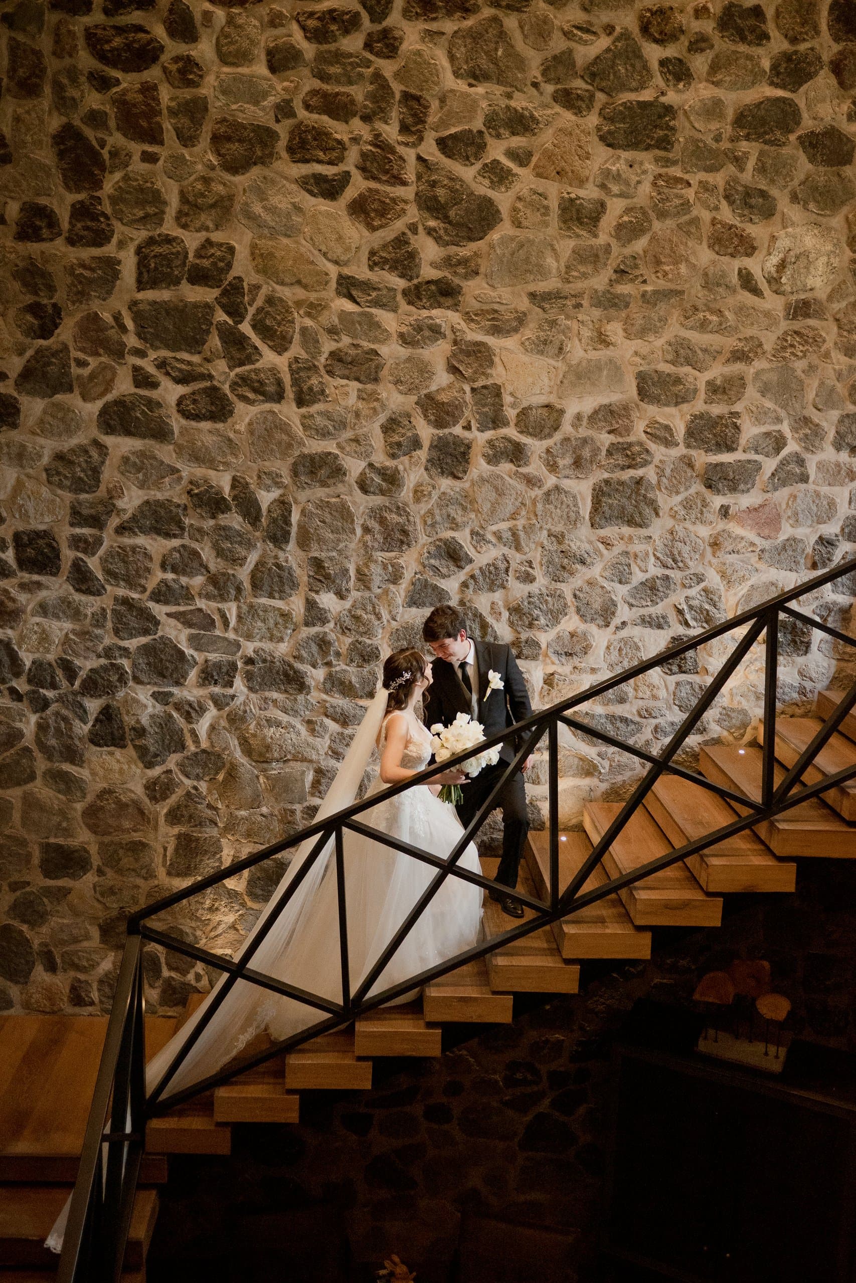Pareja abrazada en la escalera de madera de una hacienda de muro de piedra