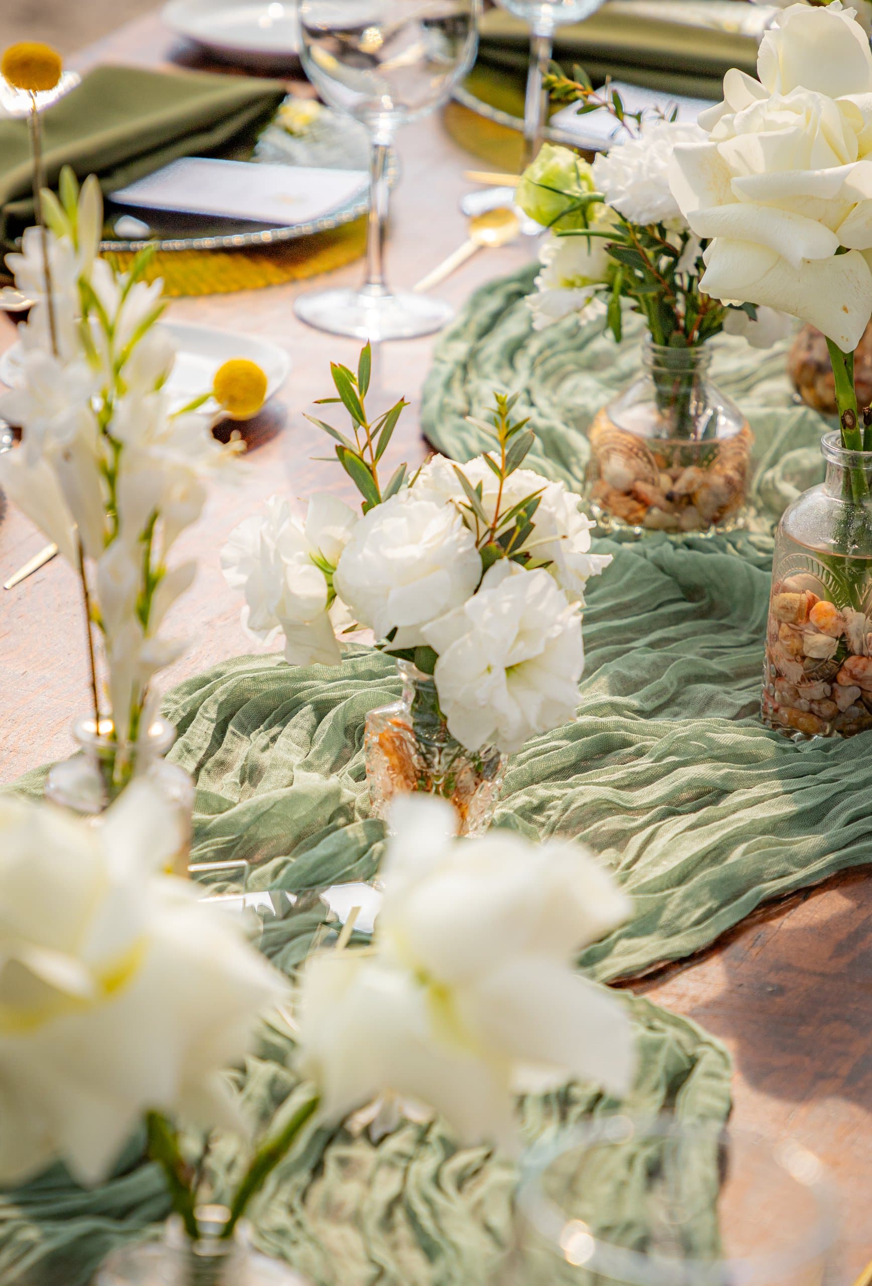 Centro de mesa con gladiolas y rosas blancas sobre camino de tela verde salvia