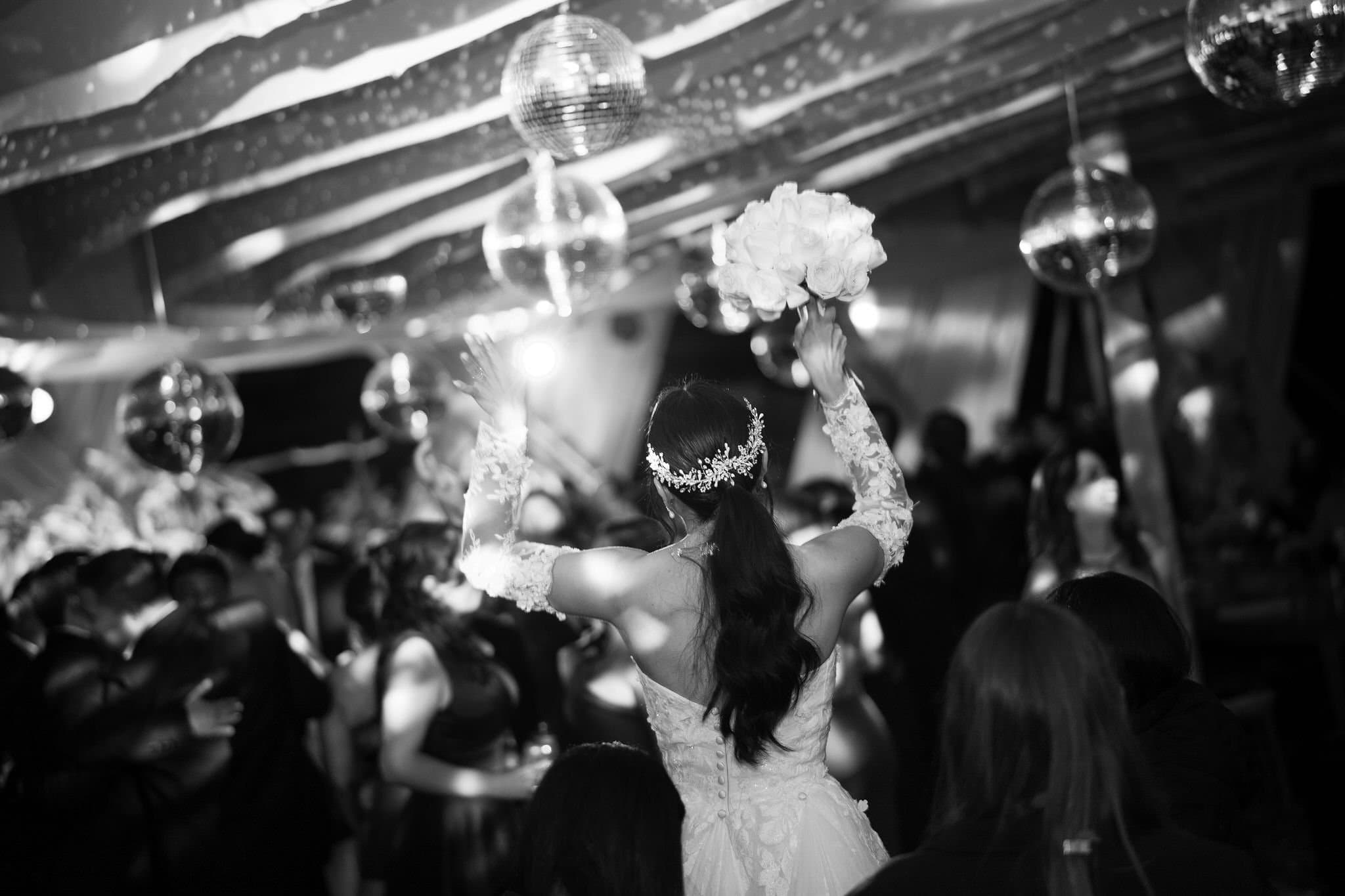 Novia lanzando el ramo en la pista bajo una esfera de espejos, en blanco y negro
