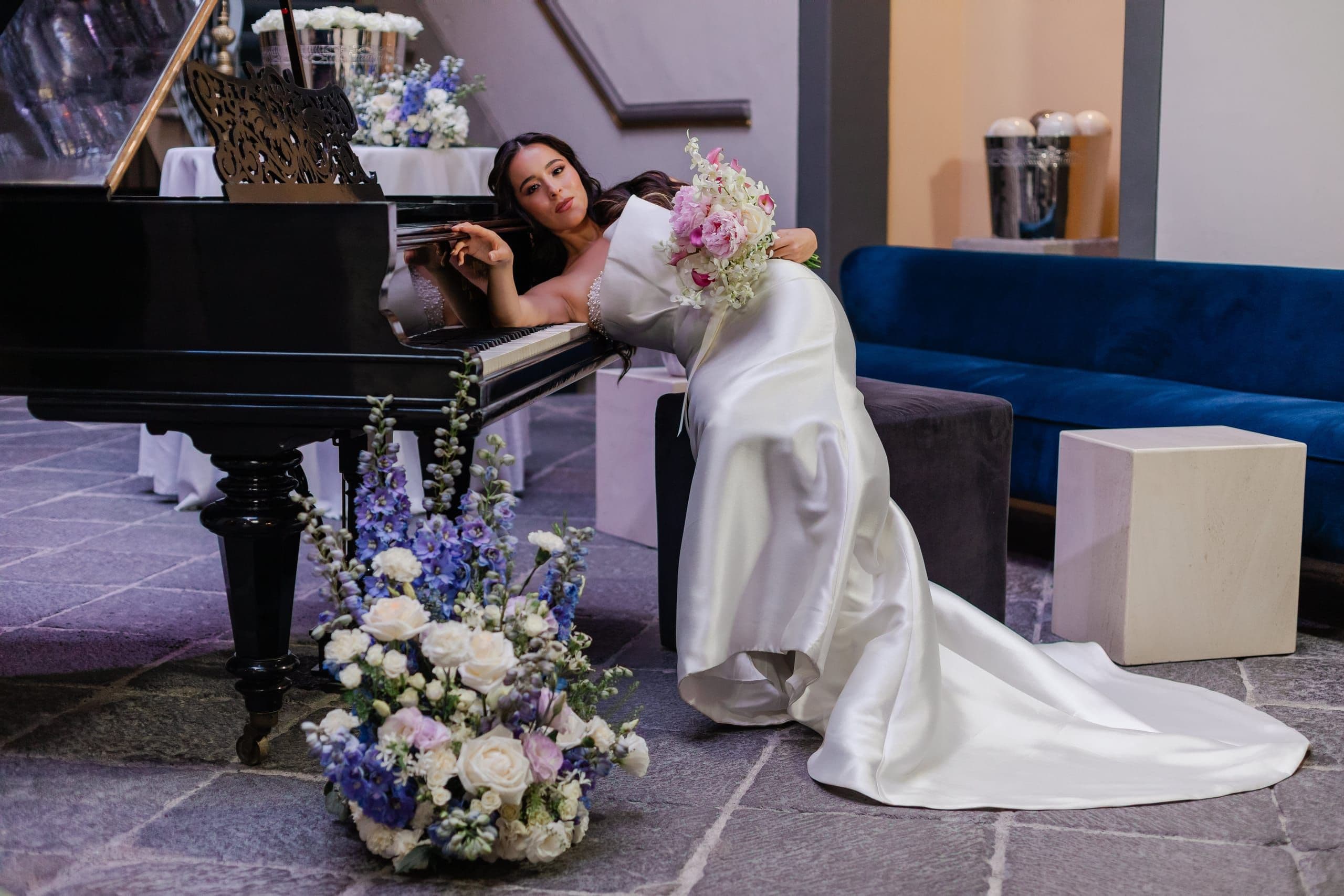 Bride resting on a grand piano beside a lavender floral arrangement, in the courtyard of a Puebla mansion