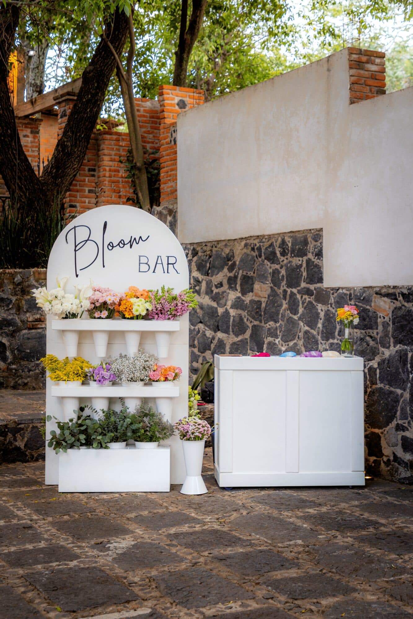 The Bloom Bar stand set up in a stone courtyard in Atlixco, flowers arranged by color before the guests arrive